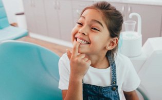 Little girl in dental chair pointing to teeth