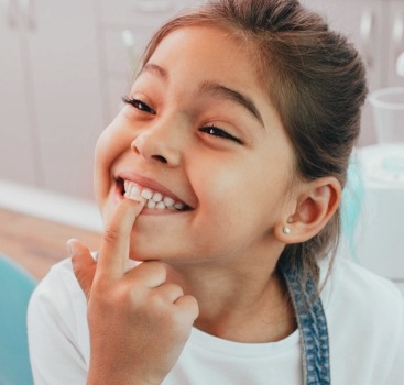 Little girl pointing to smile after dental crown restoration