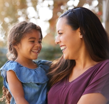 Mother holding her smiling daughter after tooth extractions