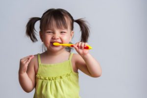 a child smiling and brushing her teeth