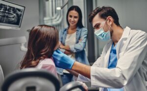 Dentist examining girl's teeth while mom looks on