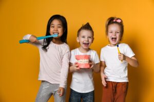 three kids using big dental instruments and smiling